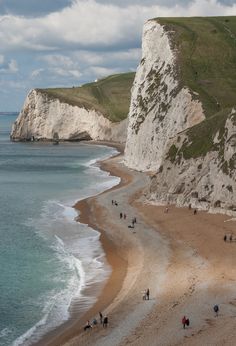 people are walking along the beach near white cliffs