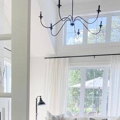 a living room filled with white furniture and lots of window sill space under a chandelier