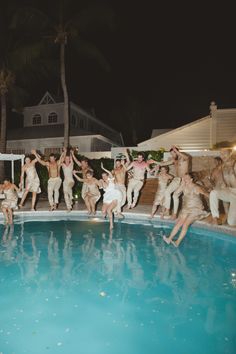 a group of people jumping into a swimming pool at night with palm trees in the background