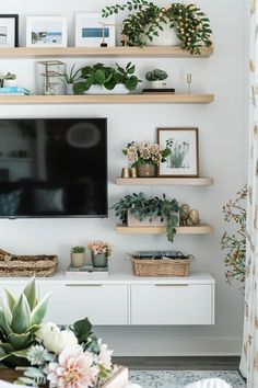 a flat screen tv sitting on top of a wooden shelf next to a plant filled wall