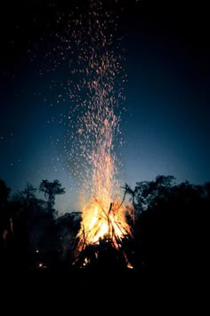 a bonfire is lit up in the dark with lots of sparks coming out of it