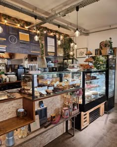 the inside of a bakery with lots of food on display and lights hanging from the ceiling