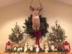 a deer head mounted on the wall above a mantle filled with candles and christmas wreaths