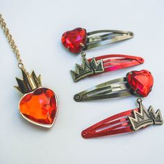 four different colored hair clips and a heart shaped brooch on a white table top