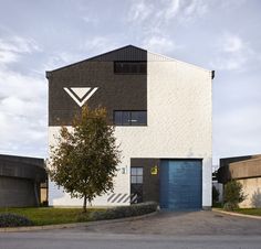 a white building with a blue door and tree in front of it on a cloudy day