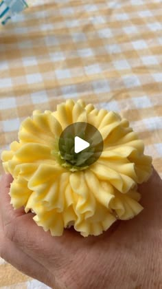 a hand holding a yellow flower on top of a checkered tablecloth covered table