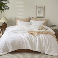 a bed with white sheets and pillows in a room next to a potted plant