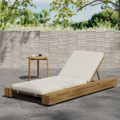 a wooden lounge chair sitting on top of a stone floor next to a brick wall