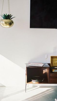 a television is hanging on the wall next to a cabinet with a plant in it