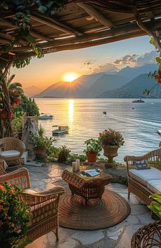 an outdoor patio with wicker furniture and flowers on the table overlooking water at sunset