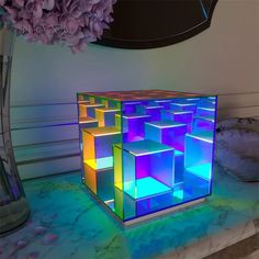 an illuminated cube is sitting on a table next to a vase with flowers in it