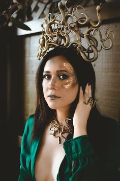 a woman wearing a gold snake headpiece and green dress with her hands on her face