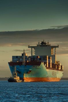 a large cargo ship in the middle of the ocean under a cloudy sky at sunset