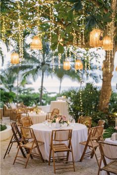 an outdoor dining area with white table cloths and lights hanging from the tree branches