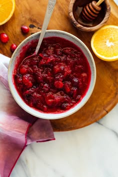 a bowl filled with cranberry sauce on top of a wooden cutting board next to sliced oranges