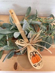 a wooden spoon with an orange painted pumpkin on it sitting next to some green leaves