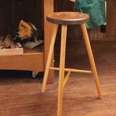 a wooden stool sitting in front of a table with tools on it and a green bag next to it