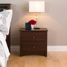 a night stand with a lamp on it next to a bed and nightstand in a bedroom