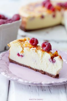 a slice of cheesecake with raspberries on top sits on a pink plate