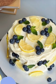 a cake with lemons, blueberries and mint leaves on it sitting on a plate