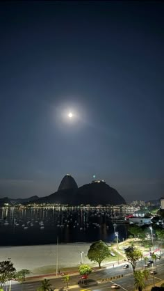 the moon is shining brightly in the night sky over a bay and mountains with boats on it