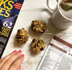 a woman's hand on top of a magazine next to cookies and a cup of tea