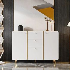 a white cabinet with gold handles in a living room area next to a mirror and lamp