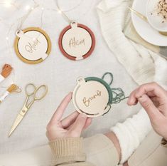 a person is holding up some personalized wooden ornaments on a table with scissors and other crafting supplies