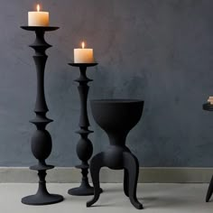 three black candlesticks sitting next to each other in front of a gray wall