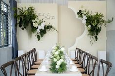 a table set up with flowers and greenery on the wall