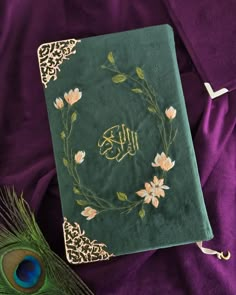 a green book with gold writing on it and a peacock feather laying next to it