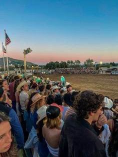 a group of people standing in front of a crowd at a horse race on a dirt field