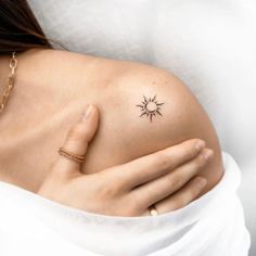 a woman's shoulder with a small tattoo on her left arm and the sun in the middle