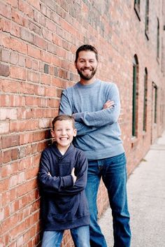 a father and son leaning against a brick wall