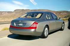 a silver car driving down the road with mountains in the background