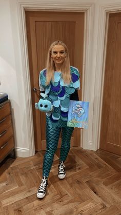 a woman is dressed as a mermaid holding two little blue fish in one hand and a book in the other