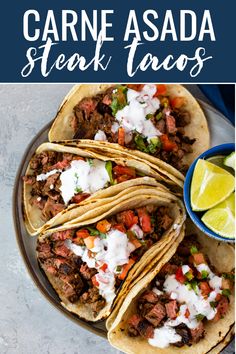 three steak tacos on a plate with lime wedges