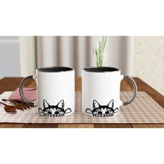 two coffee mugs sitting on top of a wooden table next to a potted plant