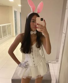 a woman taking a selfie with her cell phone wearing bunny ears and a white dress