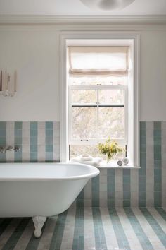 a bath tub sitting under a window next to a sink in a room with blue and white tiles