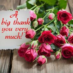 a bouquet of red roses sitting on top of a wooden table next to a sign