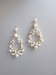 two pairs of pearl and crystal earrings on top of a white surface with one earring in the shape of a tear