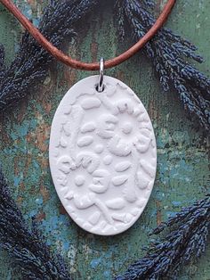 a white ceramic pendant is sitting on a brown cord and some blue flowers are in the background