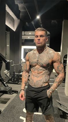 a man with tattoos standing in front of a gym machine