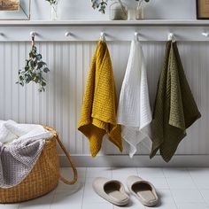 three towels hanging on the wall next to shoes and a basket filled with slippers