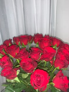 a vase filled with red roses sitting on top of a glass table next to a white curtain