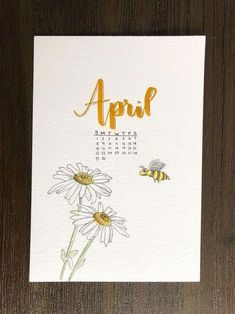 a calendar with daisies and bees on it, next to a wooden table top