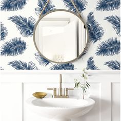 a bathroom sink under a mirror next to a wallpapered wall with blue palm leaves