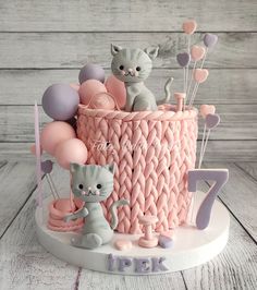 a pink and grey cat themed cake with balloons on the top is for a first birthday