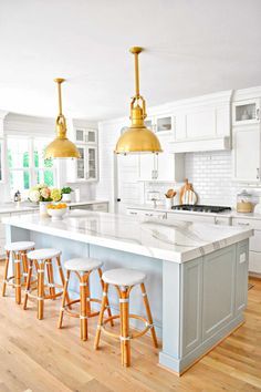 a large kitchen with white cabinets and gold pendant lights hanging from the ceiling over the island